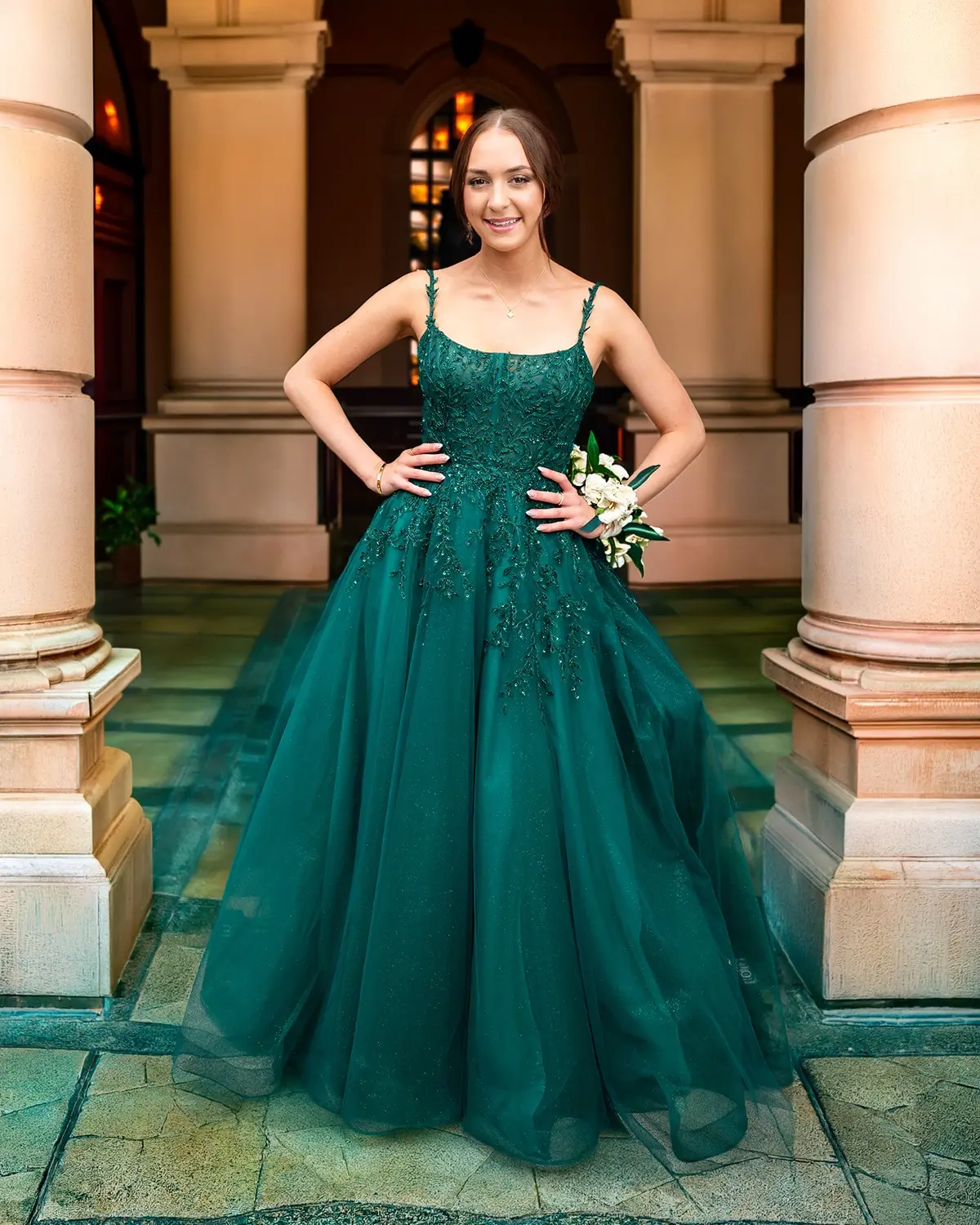 Prom attendee posing in an emerald green gown at an elegant hotel entrance