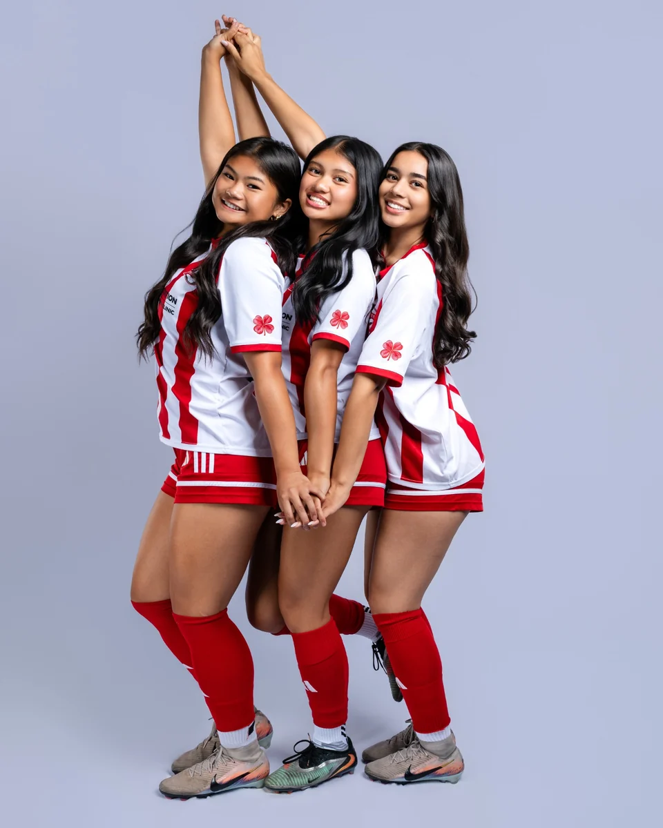 Three soccer teammates posing together in red and white uniforms
